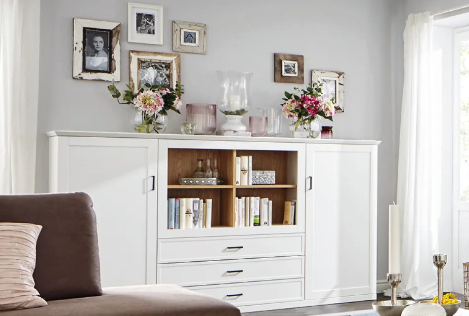 Modernes Wohnzimmer mit weißem Sideboard, offenen Regalfächern und dekorierten Blumenvasen. Wohnmöbel mit Stauraum und stilvoller Wanddekoration für eine helle Wohnzimmereinrichtung